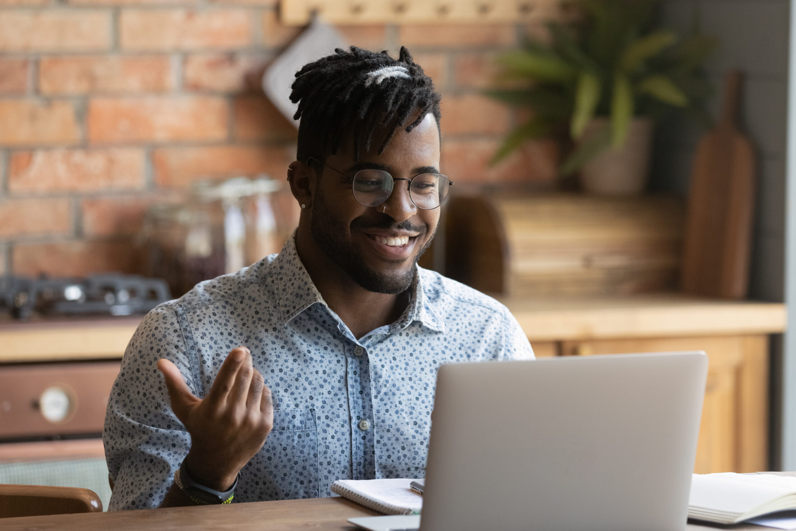 A man gestures and smiles while looking at a laptop screen.